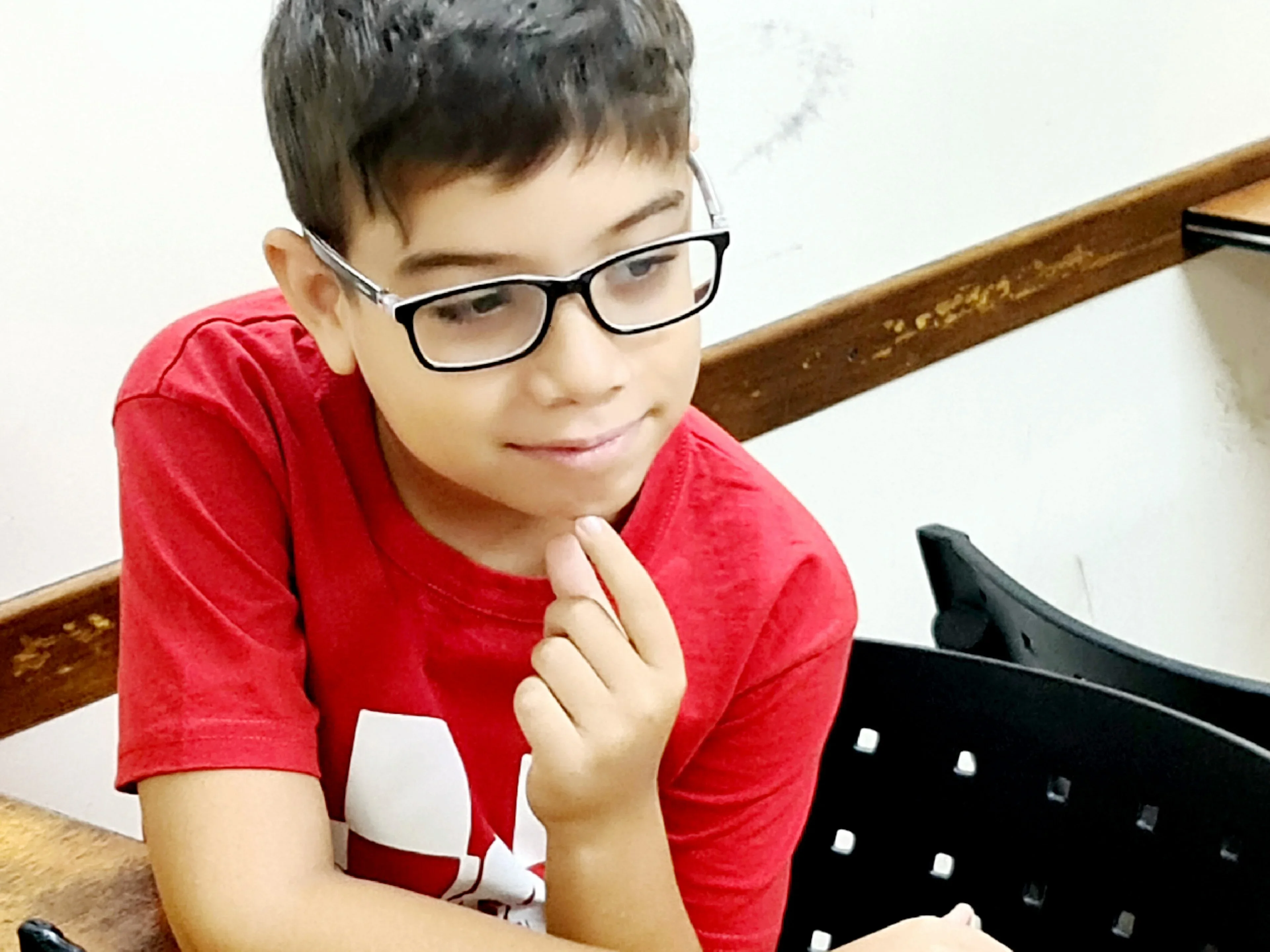 A young Faustino Oro in a red t-shirt and glasses smiling over a chessboard