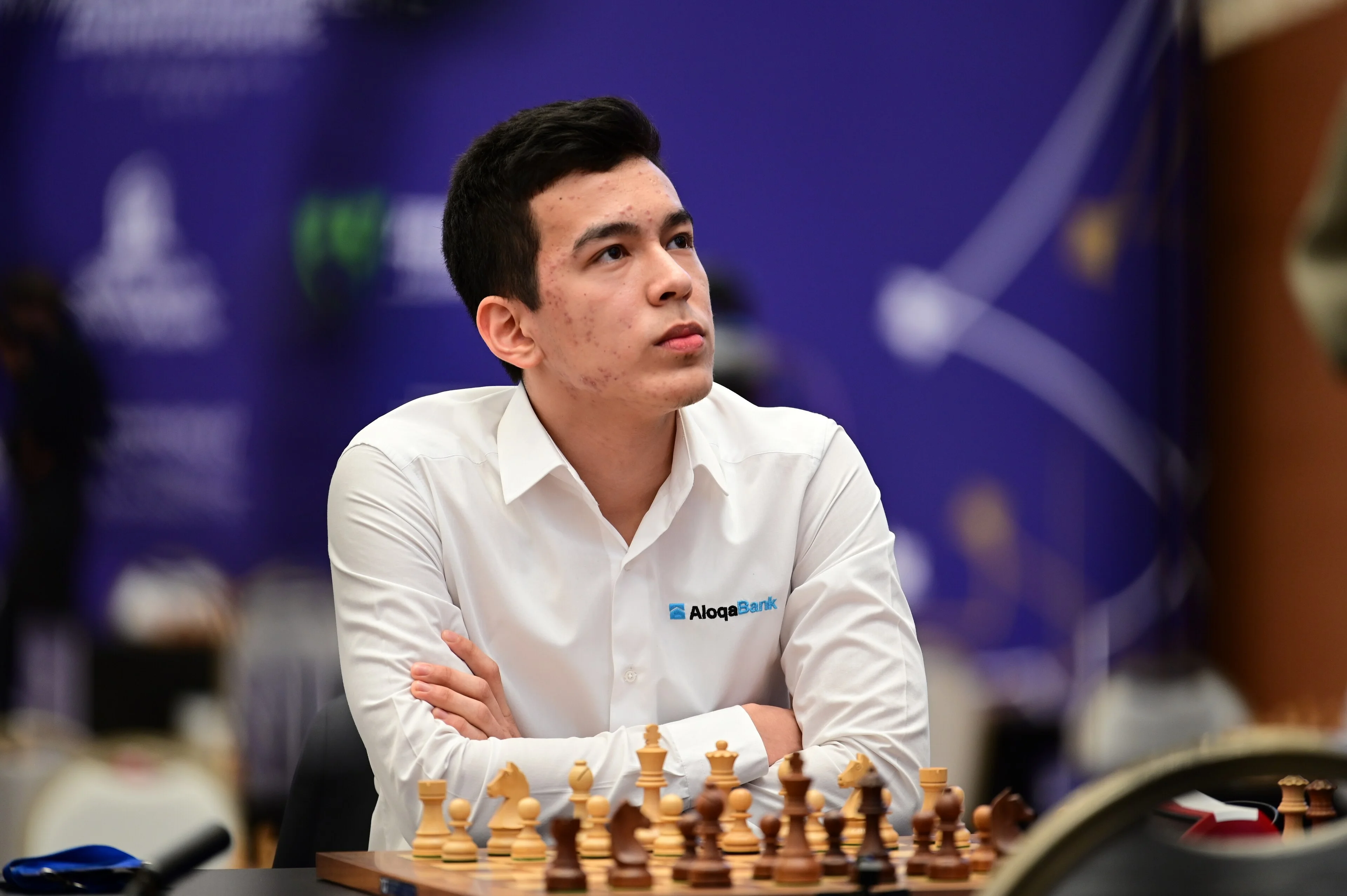 Nodirbek Abdusattorov seated at a chessboard with arms crossed during a tournament