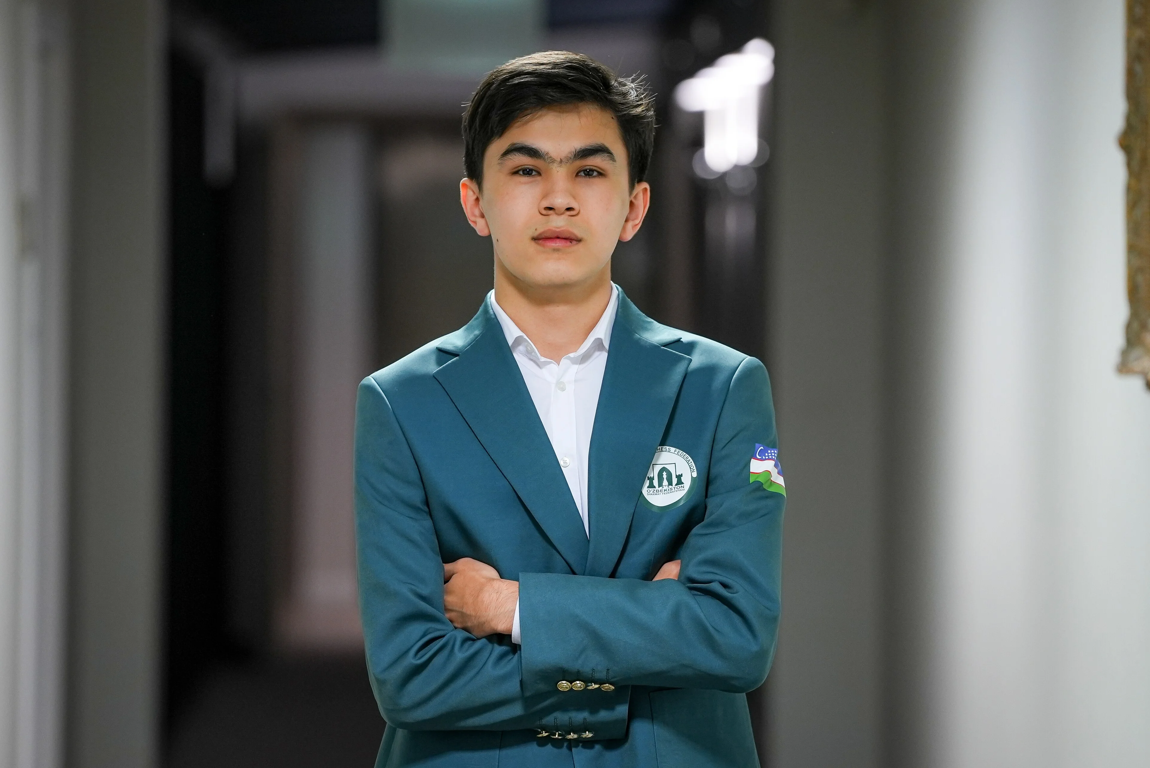 Javokhir Sindarov standing with arms crossed in an Uzbekistan team blazer